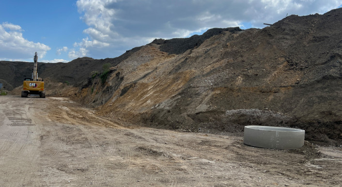 Mülldeponie. Erdhügel. Auf der linken seite ein gelber Bagger.