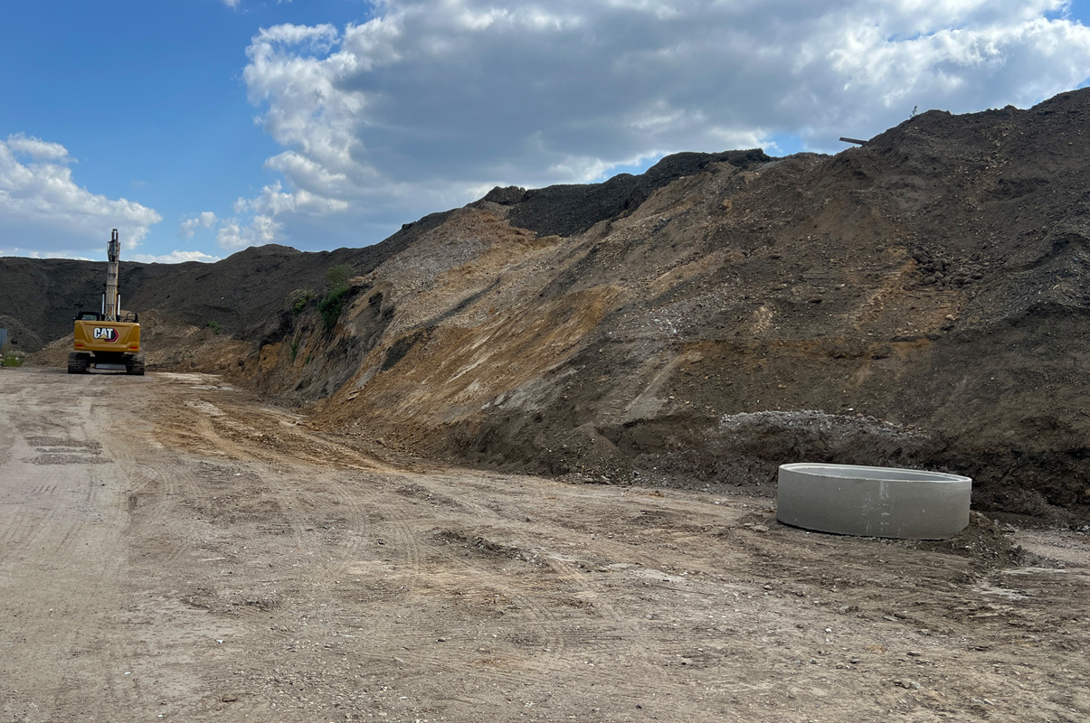 Mülldeponie. Erdhügel. Auf der linken seite ein gelber Bagger.