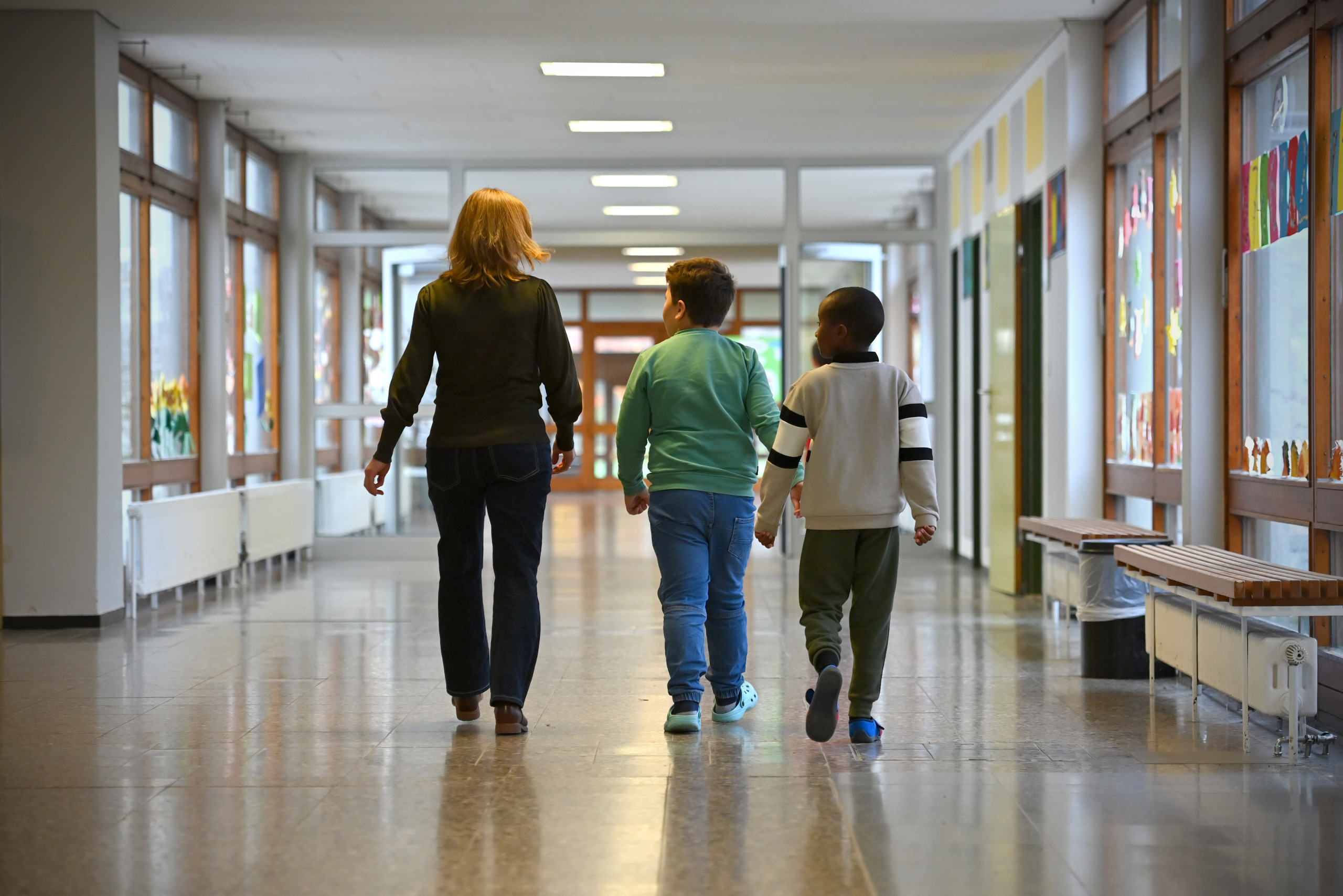 Eine erwachsene Person und zwei Kinder laufen einen Flur entlang.
