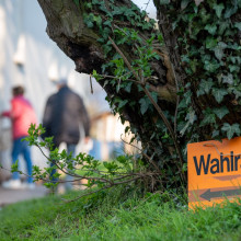 Wahlen in Deutschland: Schild mit der Aufschrift Wahlraum steht vor einem Baum - im Hintergrund sind Menschen und ein Gebäude zu sehen