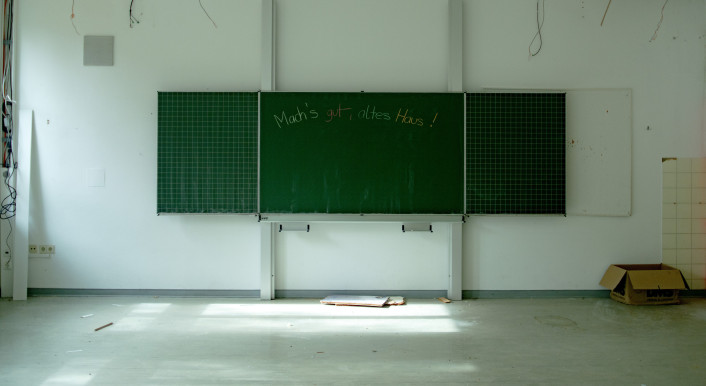 Leeres Klassenzimmer eines leergeräumten Schulgebäudes. AUf der Tafel steht: „Mach's gut altes Haus."