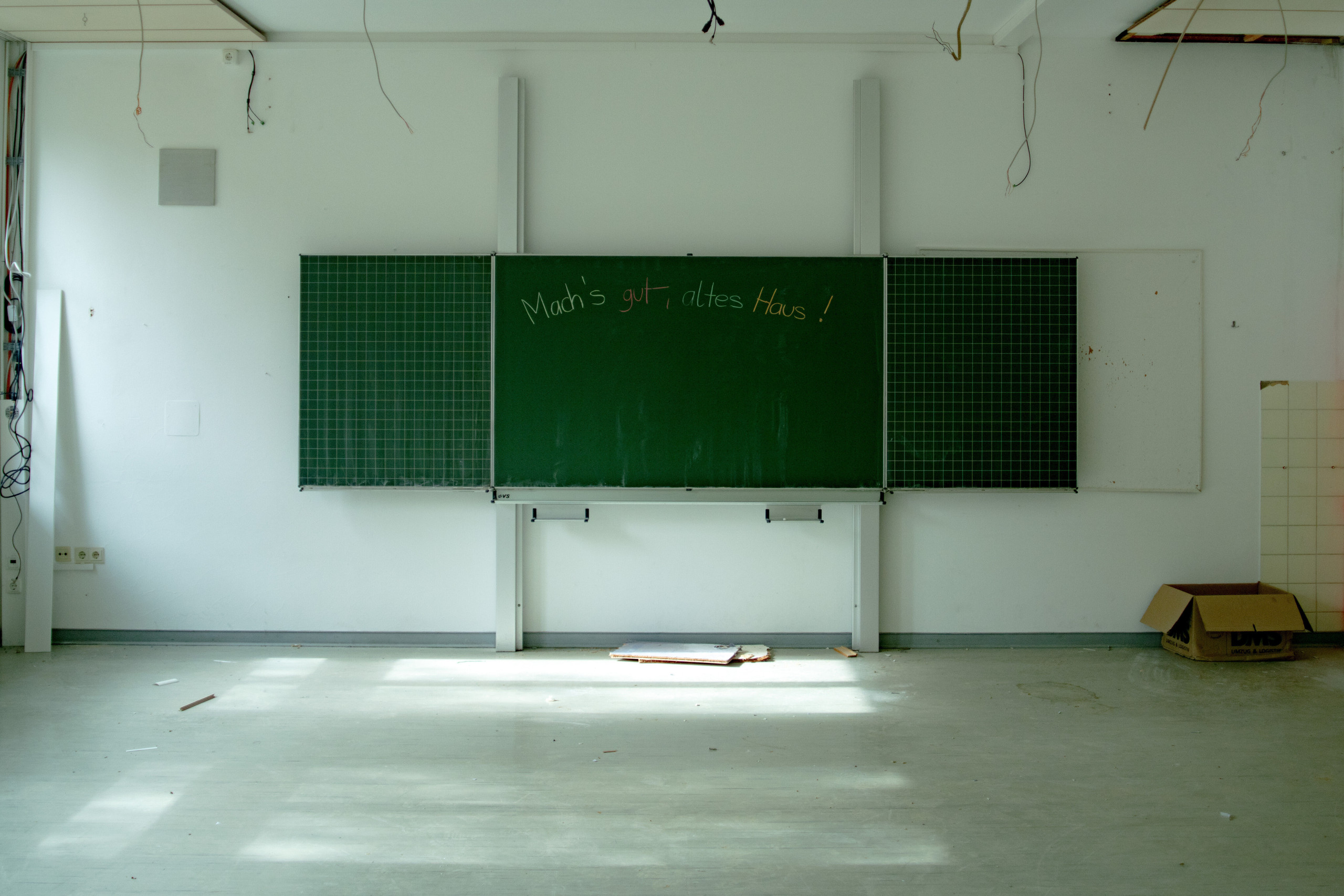 Leeres Klassenzimmer eines leergeräumten Schulgebäudes. AUf der Tafel steht: „Mach's gut altes Haus."