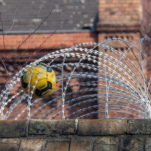 Ein Fußball steckt in dem Sicherheitszaun auf der Mauer der Jugendstrafanstalt Berlin.