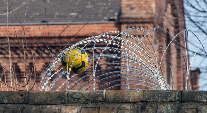 Ein Fußball steckt in dem Sicherheitszaun auf der Mauer der Jugendstrafanstalt Berlin.