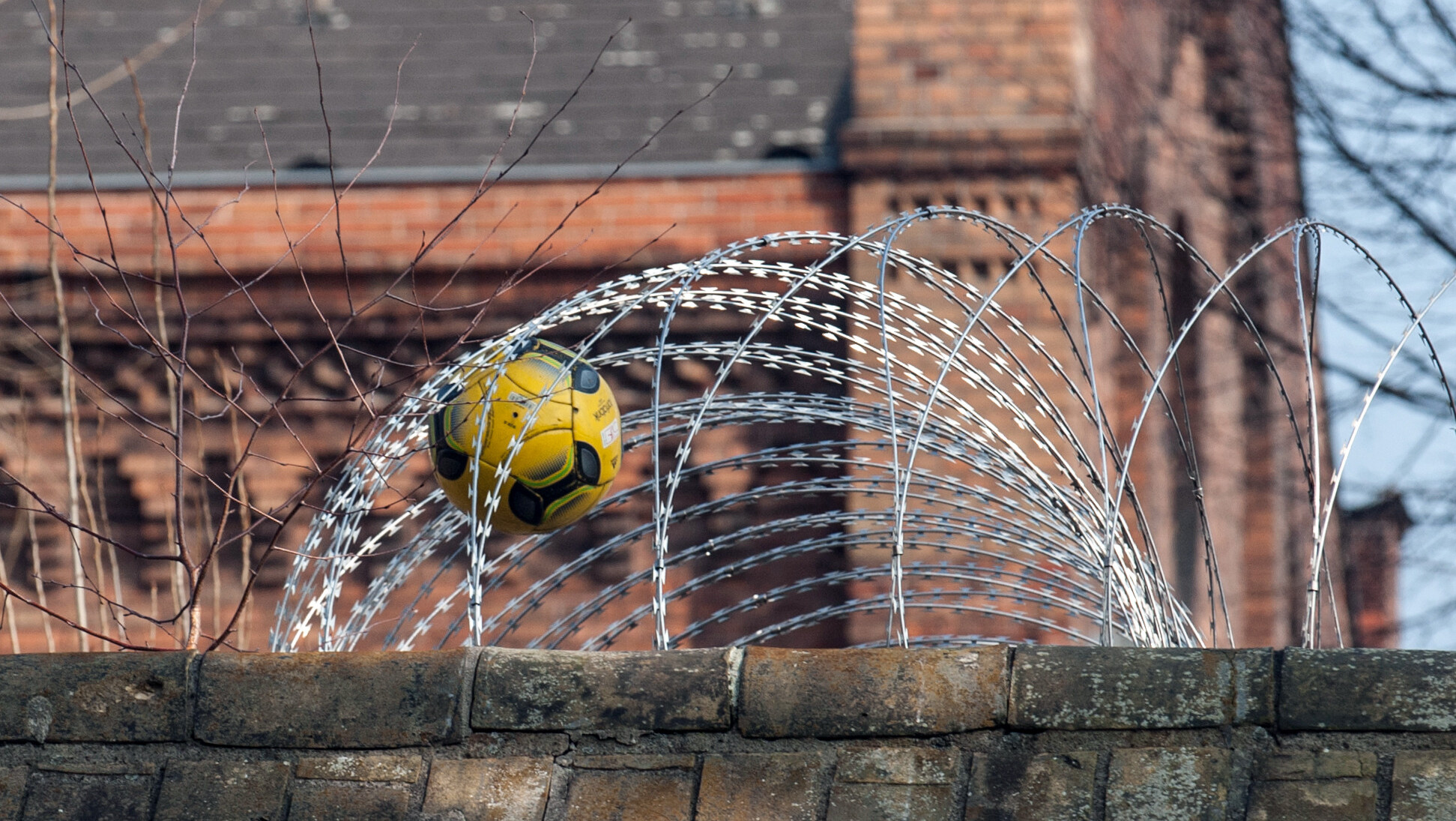 Ein Fußball steckt in dem Sicherheitszaun auf der Mauer der Jugendstrafanstalt Berlin.