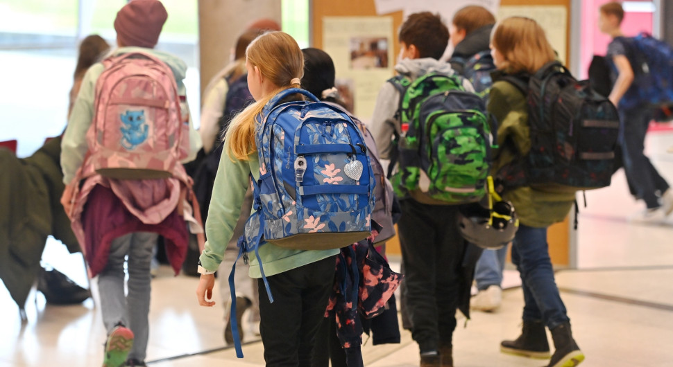 Kinder laufen mit Schulränzen auf dem Rücken durch einen Raum.