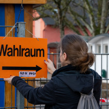 Frau hängt Schild zum Wahlraum bei der Landtagswahl in Rheinland-Pfalz im März 2026 auf