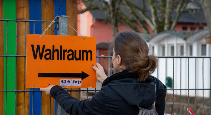 Frau hängt Schild zum Wahlraum bei der Landtagswahl in Rheinland-Pfalz im März 2026 auf