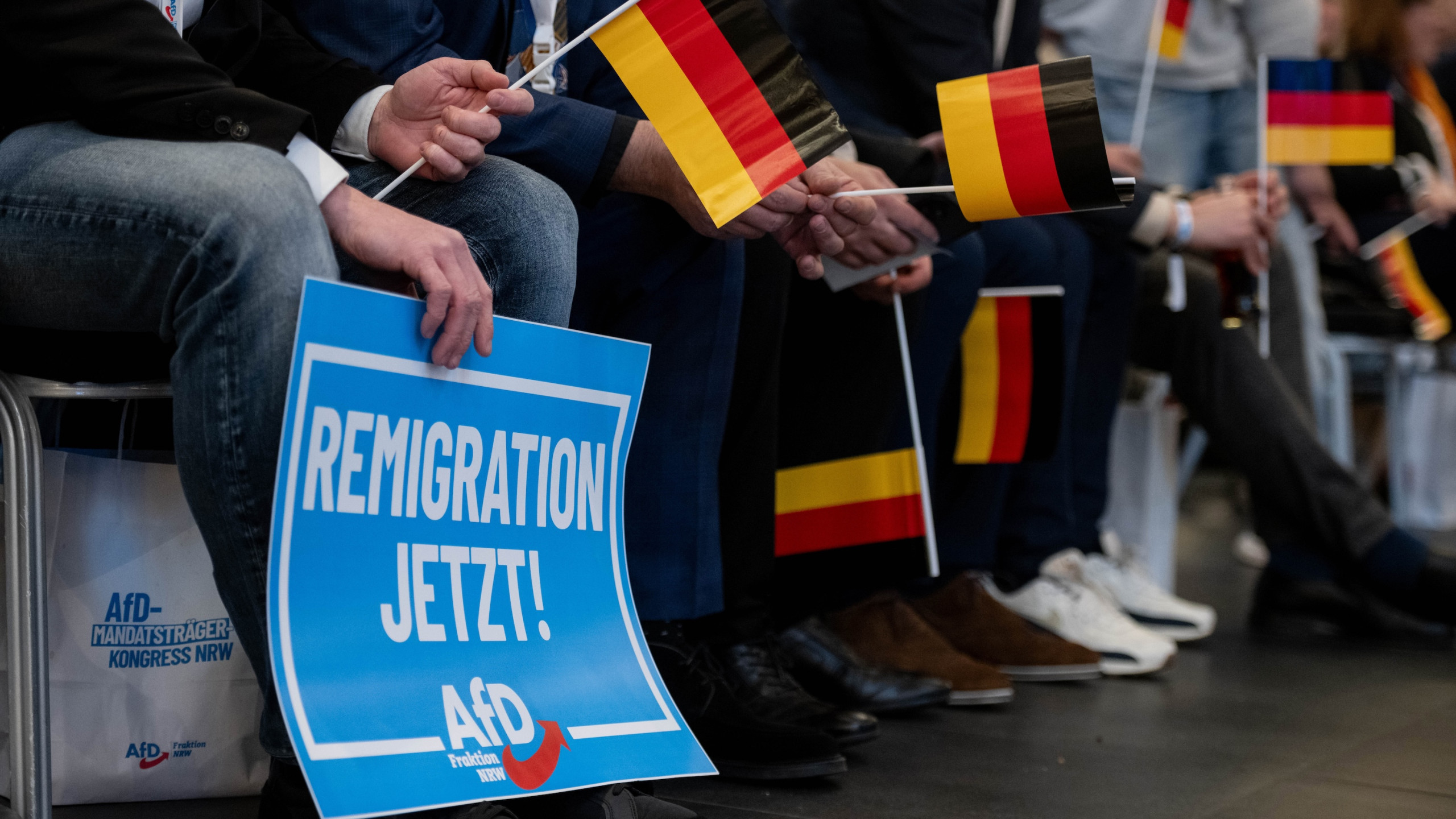Teilnehmer vom Mandatsträgerkongress halten Deutschlandfahnen und ein Schild, auf dem „Remigration jetzt!“ steht.