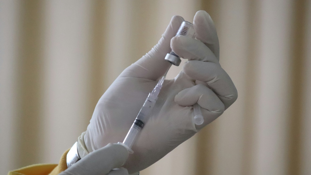 Hand hält aufgezogene Spritze, an deren Kanüle sich ein Tropfen bildet