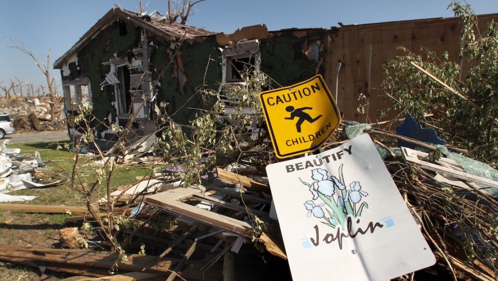 Ein umgefallenes Schild vor einem durch den Tornado zerstörtem Haus