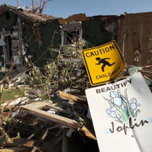 Ein umgefallenes Schild vor einem durch den Tornado zerstörtem Haus