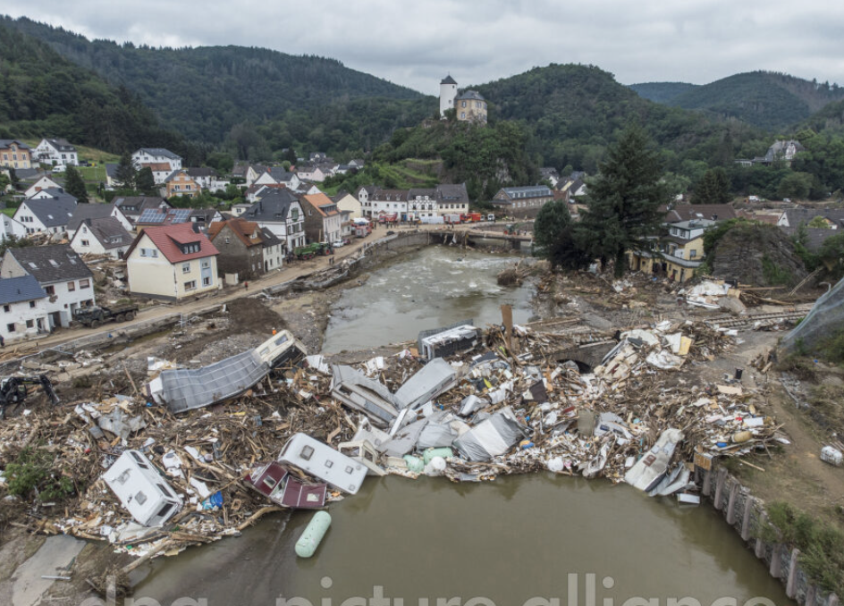 Das Bild zeigt eine Drohnenaufnahme vom 19. Juli 2021. Zu sehen sind meterhoch aufgetürmte Trümmer – Wohnwagen, Gastanks, Bäume und Schrott – an der zerstörten Brücke über die Ahr in Altenahr-Kreuzberg wenige Tage nach der Flutkatastrophe. (Bild: picture alliance/dpa | Boris Roessler)
