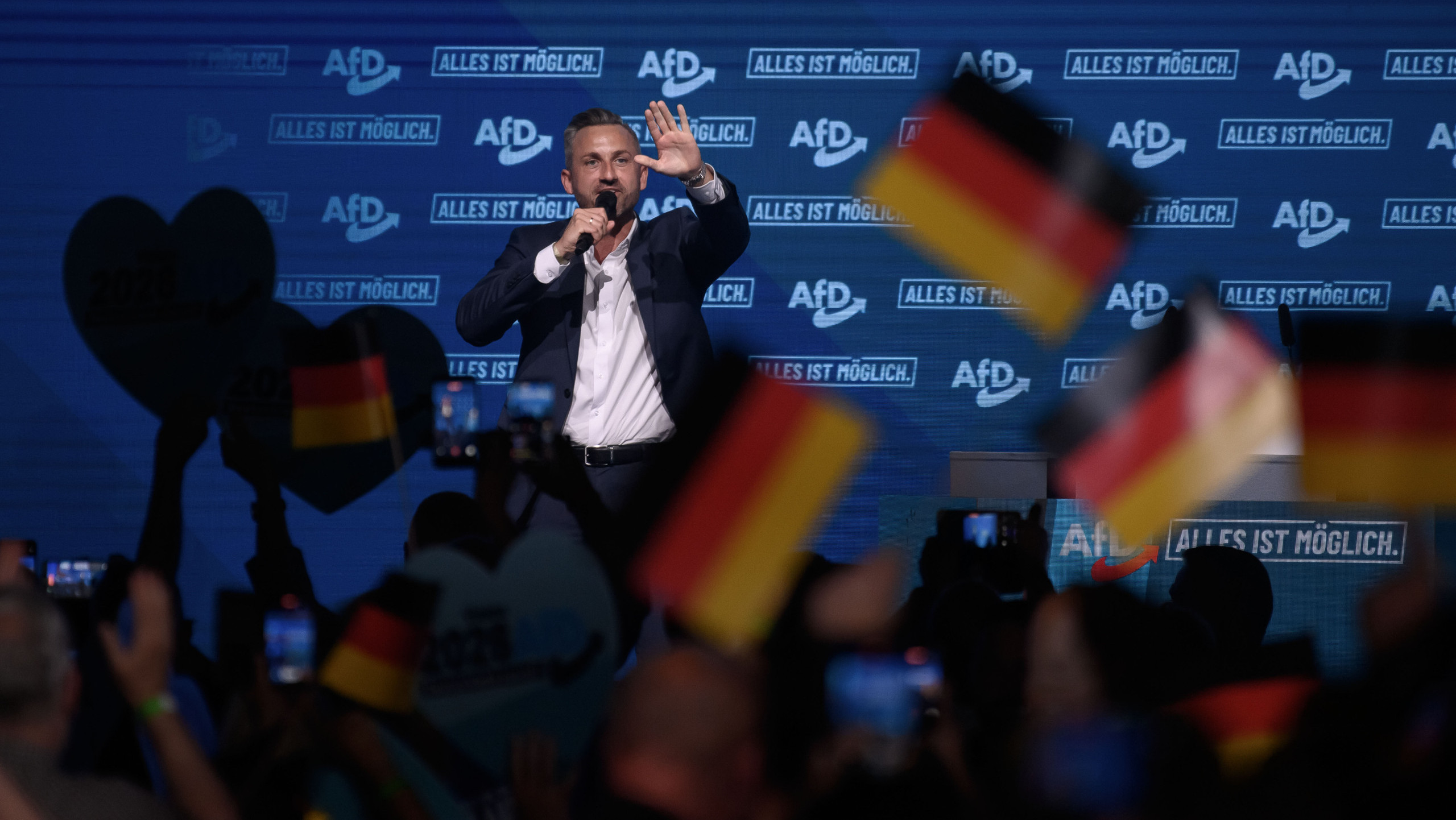 Der AfD-Spitzenkandidat für die Landtagswahl Ulrich Siegmund steht auf einer Bühne. Er trägt Anzug. Im Vordergrund und zur Kamera mit dem Rücken zugewandt ist eine Menschenmenge, die ihm zujubelt.