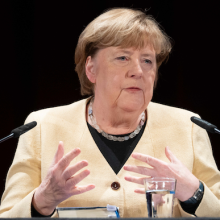 Angela Merkel sitzt vor zwei Mikrofonen.