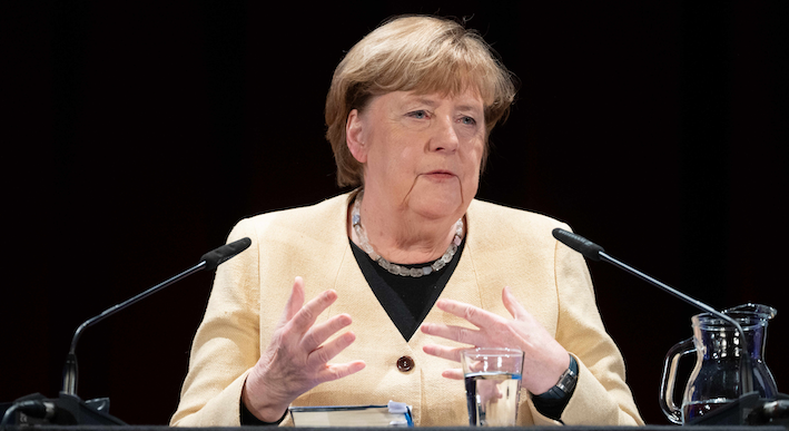 Angela Merkel sitzt vor zwei Mikrofonen.