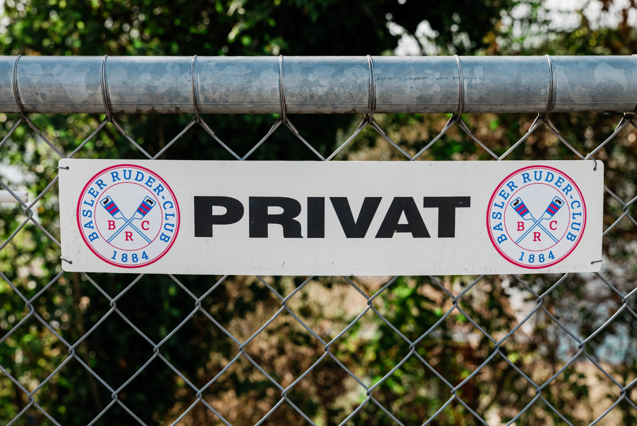 Schild mit der Aufschrift „Privat“ und den Logos des Basler Ruder-Clubs von 1884 an einem Maschendrahtzaun.
