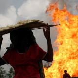 Ein nigerianisches Mädchen trägt ein Brett mit Tapioka auf dem Kopf an einer hohen Gasfackel vorbei.