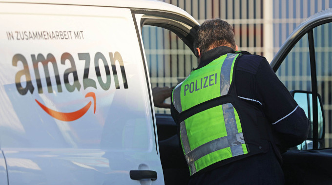 Ein Polizist mit gelber Warnweste kontrolliert ein Amazon Kurierfahrer, der bei einem Subunternehmen angestellt ist.